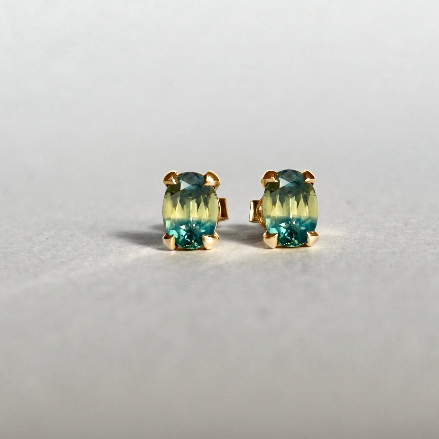 A pair of oval cut parti sapphires in an 18ct yellow gold stud setting 